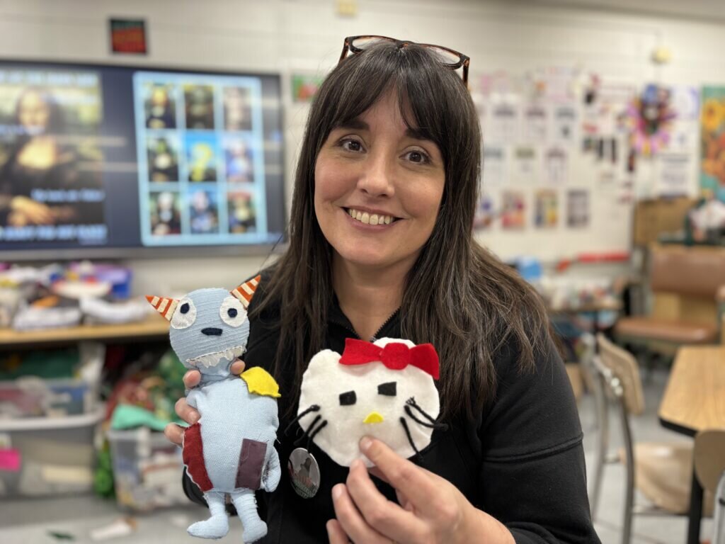 Picture of staff member Michelle T holding 2 stuffed objects that was made by students. 
