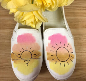 White canvas shoes with a sunset painted on each shoe.
