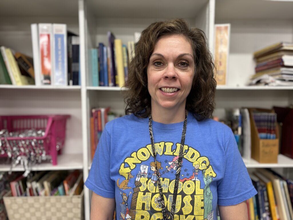 Drama teacher at Cooper, Heather Renkar, smiles for a photo in front of a bookshelf.